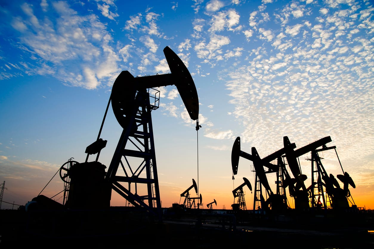 Oil pumpjacks silhouetted against a blue sky with scattered clouds