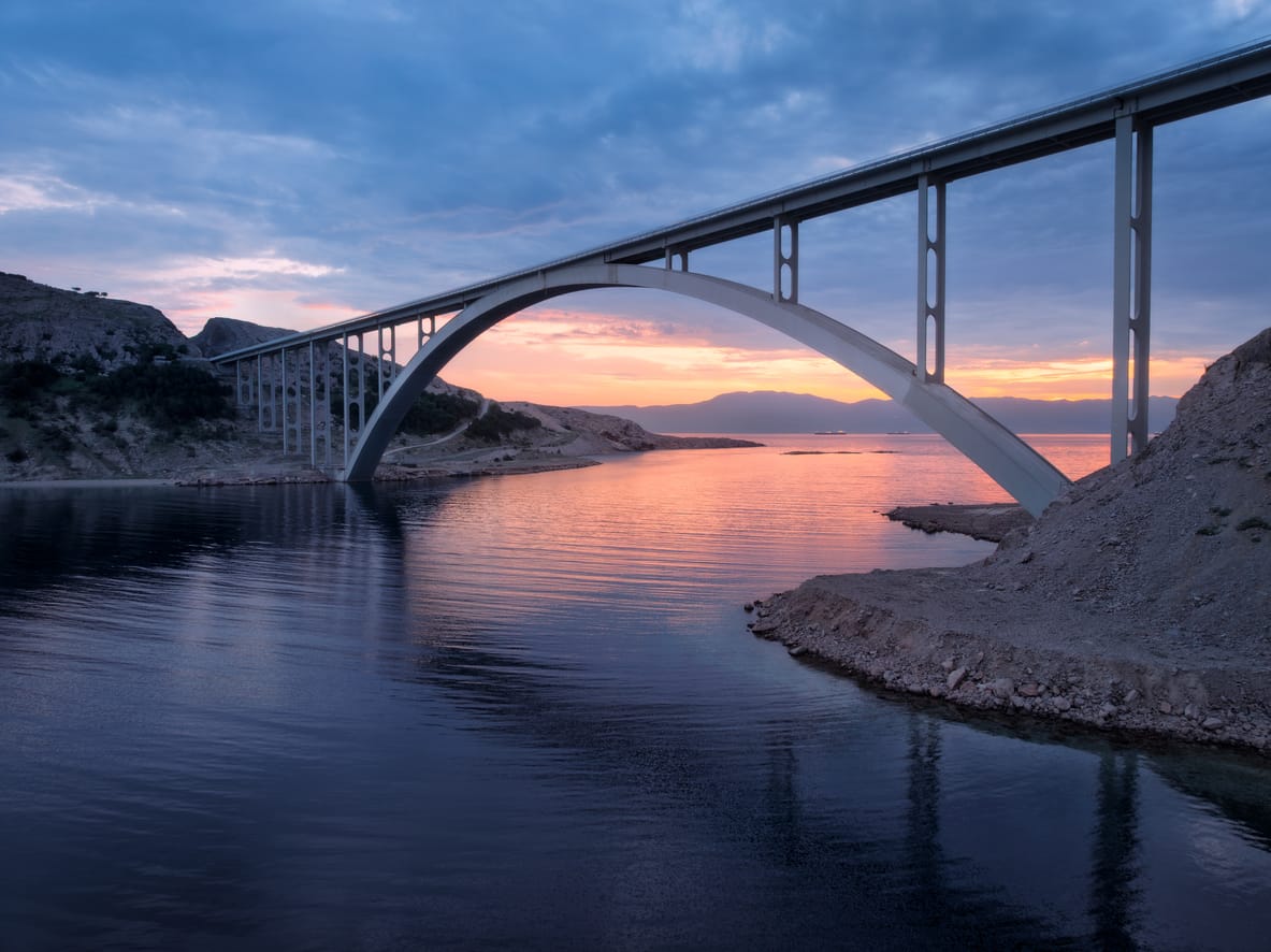 A large arch bridge over calm water at sunset