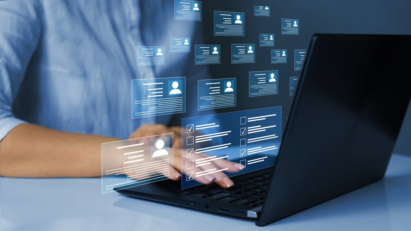 Hands typing on a laptop with digital profile cards and checklists floating above the keyboard